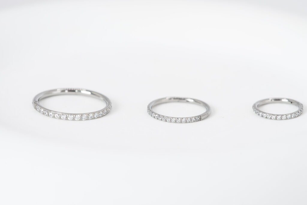 Cliker en titanio con zirconias brillantes, disponible en medidas de 6 mm, 8 mm y 10 mm. Una joya elegante y versátil para tu piercing.